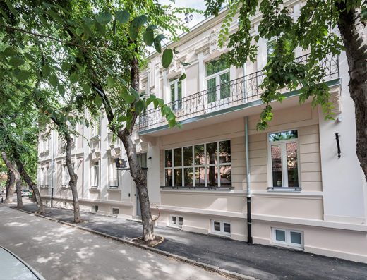 Spoljašnjost Artist Hotel Subotica sa belom klasičnom fasadom, balkonom sa kovanom ogradom i drvoredima na ulici