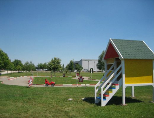 Dečije igralište u Autokomerc Karting Centar sa mini karting stazom, dečijim automobilom, drvenom kućicom i zelenim travnjakom