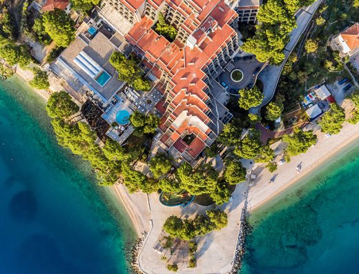 Aerijalni pogled na Bluesun hotel Soline sa crvenim krovovima, bazenima, borovom šumom i tirkiznim morem sa obe strane