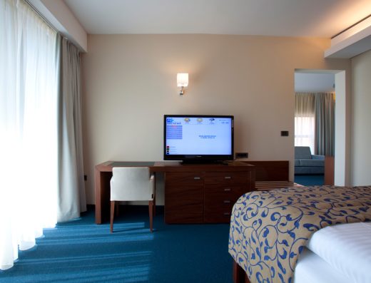 Apartman u Bohinj Park Eco Hotel sa TV-om, radnim stolom, plavim tepihom i dnevnom sobom u pozadini