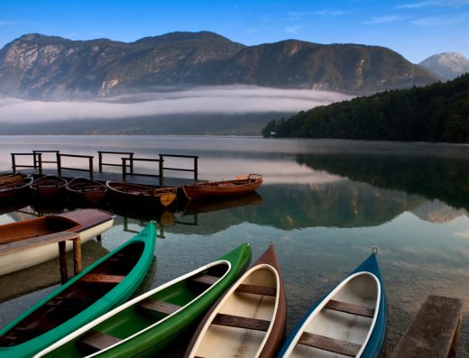 Bohinjsko jezero u blizini Bohinj Park Eco Hotel sa čamcima i kanuima na obali, drvenim molom i jutarnjom maglom iznad planina