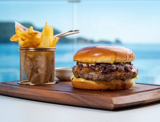 Burger sa karamelizovanim lukom i pomfritom na drvenoj dasci u Dukley Seafront Restaurant and Beach sa pogledom na more