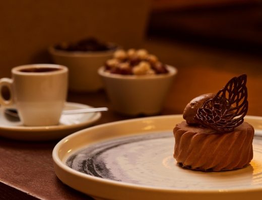 Detalj čokoladnog deserta u Grey Hotel Kopaonik sa dekorativnim čokoladnim krilom, espresso kafom i činijom oraaha u toplom ambijentu