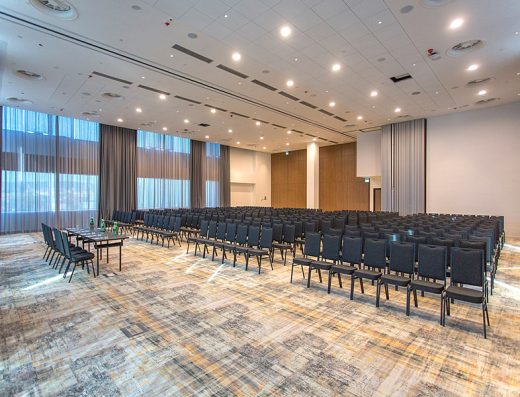 Balska dvorana u Hilton Conference and Event Center Zagreb sa tamnim stolicama u teatar rasporedu, visokim zavesama, panoramskim prozorima i drvenim panelom na bini