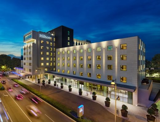 Spoljna fasada Hilton Podgorica Crna Gora hotela noću sa osvetljenom zgradom i prometnom ulicom u prvom planu