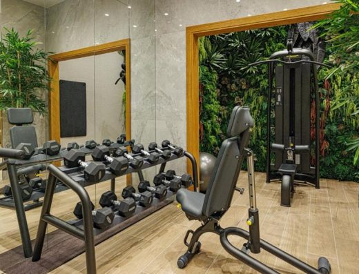 Fitnes sala u Hotel Balkan sa stalkom za bučice, spravama za vežbanje, vertikalnim zelenim zidom i velikim ogledalom