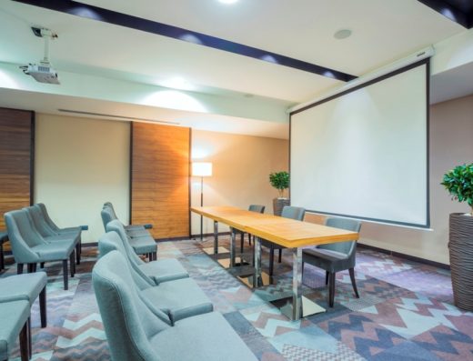 Konferencijska sala u Hotel Constantine the Great sa sivim foteljama, projektorom, platnom i drvenim panelima na zidovima