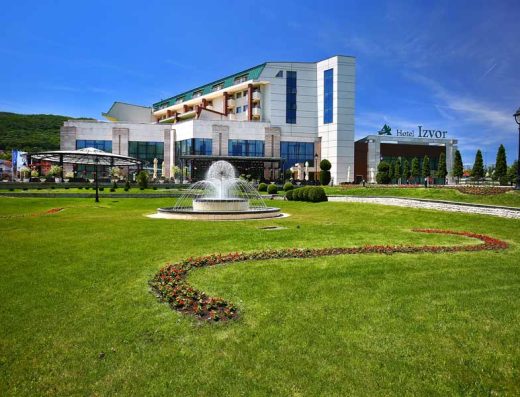 Spoljašnjost Hotel Izvor sa fontanom, zelenim travnjakom, cvećem i natpisom na fasadi
