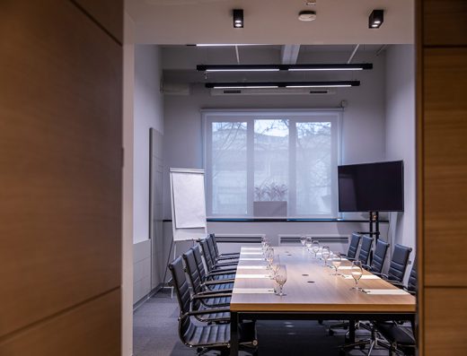 Boardroom sala u Hotel Mona Plaza sa drvenim stolom, crnim kožnim stolicama, TV ekranom i flipčartom