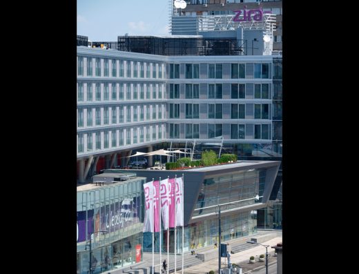 Fasada Hotel Zira Beograd danju sa modernom staklenom arhitekturom, natpisom Zira na krovu, ružičastim zastavama i zelenom terasom na krovu