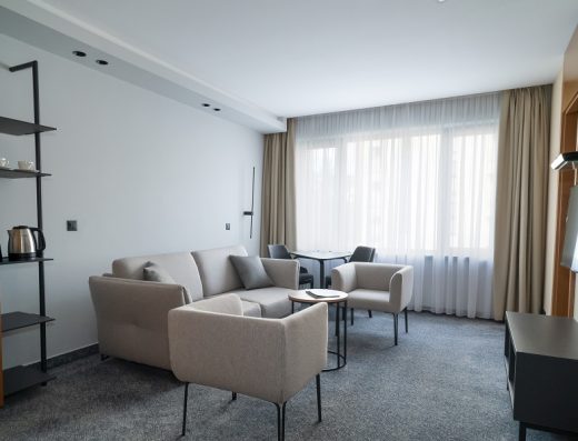 Dnevna soba apartmana u Hotel Zlatibor Mona sa bež kaučom i foteljama, stočićem za kafu, policom sa ketlerom, plavim tepihom i velikim prozorom
