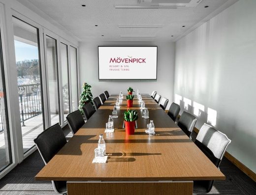 Boardroom sala u Mövenpick Resort & Spa Fruške Terme sa dugačkim drvenim stolom, crnim stolicama, ekranom sa logom i panoramskim prozorima sa zimskim pogledom