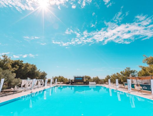 Bazen u Obonjan Island Resort Croatia sa binom, baldahinima, ležaljkama i brendiranim zastavama na sunčanom danu
