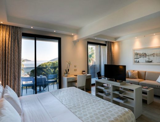 Soba sa bračnim krevetom u Palmon Bay Hotel & Spa sa TV-om, sofom, radnim stolom i balkonom sa pogledom na more i palme