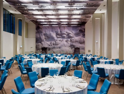 Balna sala u Radisson Blu Resort Split sa okruglim stolovima postavljenim za banket, plavim stolicama, belim stolnjacima i kamenim muralima