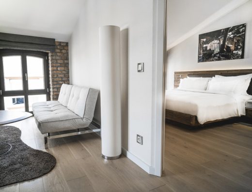 Apartman u hotelu Radisson Collection Hotel Old Mill Belgrade sa dnevnom sobom, sivim kaučem, ciglenim zidom, prozorima i spavaćom sobom vidljivom kroz pregradu