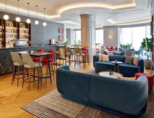 Bar u Sheraton Zagreb Hotelu sa plavim plišanim kaučima, crvenim barskim stolicama, policama sa pićima i visećim svetiljkama