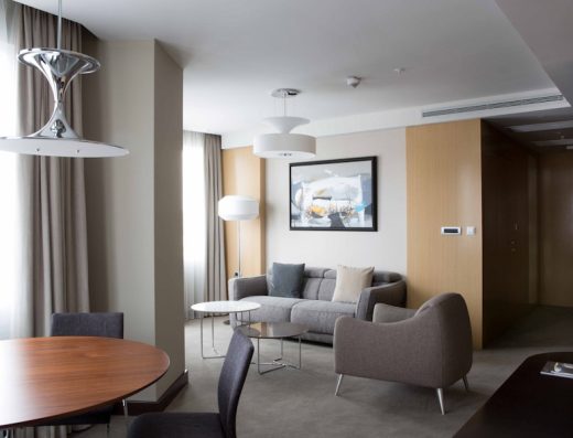 Apartman u Skopje Marriott Hotel sa sivom sofom, foteljom, okruglim trpezarijskim stolom, hromiranom lampom, umetničkom slikom i drvenim panelima