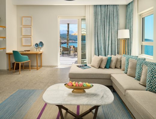 Dnevna soba apartmana u The Chedi Luštica Bay sa ugaonom sofom, tirkiznim jastucima, mermernim stolom i pogledom na more sa terase