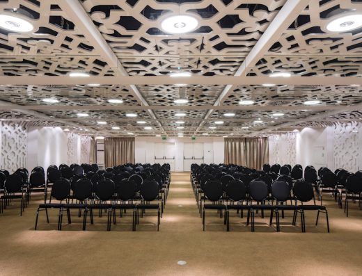 Balna sala u Zijin Hotel Belgrade sa crnim stolicama u teatarskom rasporedu, dekorativnim ornamentalnim plafonom, belim pregradama i bež zavesama